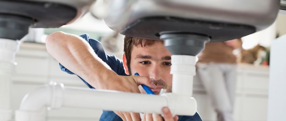 Plumber repairing pipes under a kitchen sink